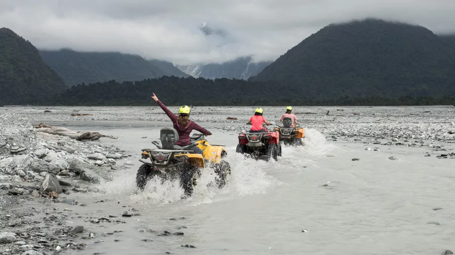 Riders on quad bikes crossing glacial rivers near Franz Josef Glacier on New Zealand’s West Coast