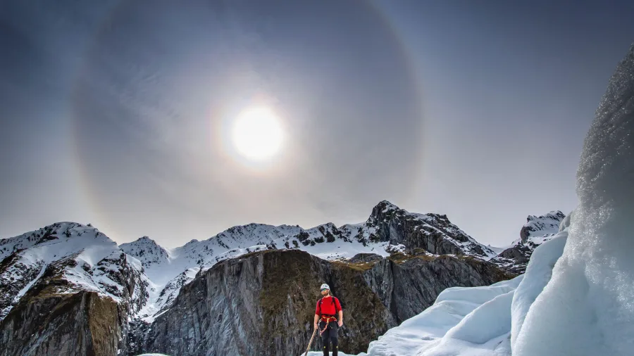Person helihiking on Fox Glacier under a bright sun halo in the Southern Alps