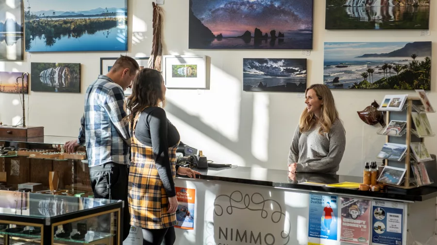 Visitors chatting with a staff member inside Nimmo Gallery Store in Greymouth, surrounded by local photography and art displays