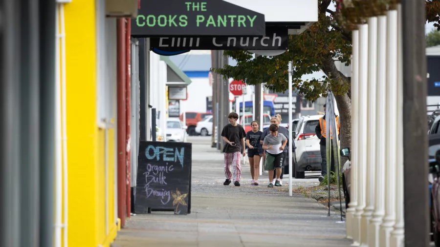 People walking past The Cooks Pantry organic shop on a main street in Greymouth, West Coast, New Zealand