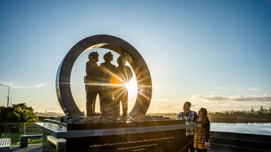 Couple standing in front of the Miners' Memorial in Greymouth at sunset, honouring those lost in West Coast coal mining incidents