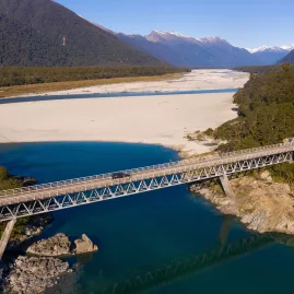 Aerial view of the bridge crossing the Arawata River with turquoise water and alpine ranges in the background