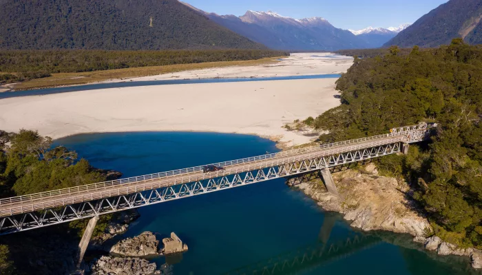 Aerial view of the bridge crossing the Arawata River with turquoise water and alpine ranges in the background
