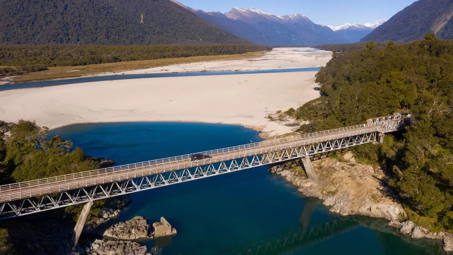 Aerial view of the bridge crossing the Arawata River with turquoise water and alpine ranges in the background