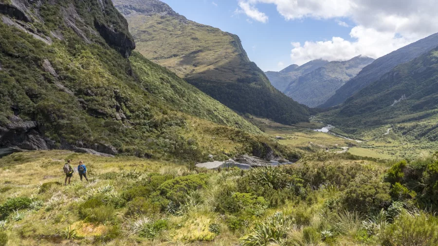 Two hikers walking through Haast back country surrounded by dramatic alpine valleys and native bush