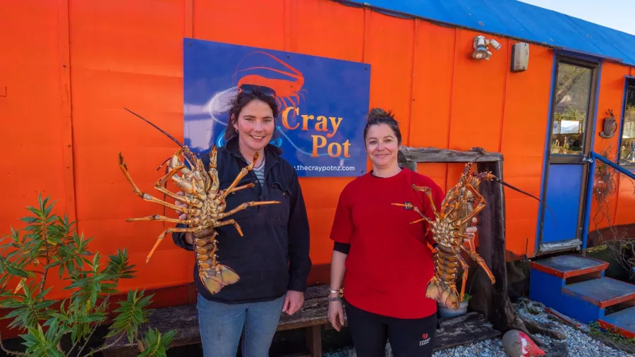 Two women holding freshly caught crayfish outside The Cray Pot in Jackson Bay on New Zealand’s West Coast