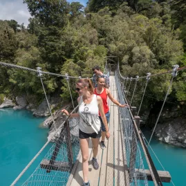 Group of people crossing the swing bridge over Hokitika Gorge with turquoise water below