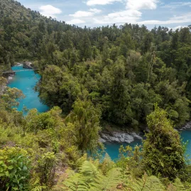 View of Hokitika Gorge with turquoise river, lush forest, and a swing bridge in the distance