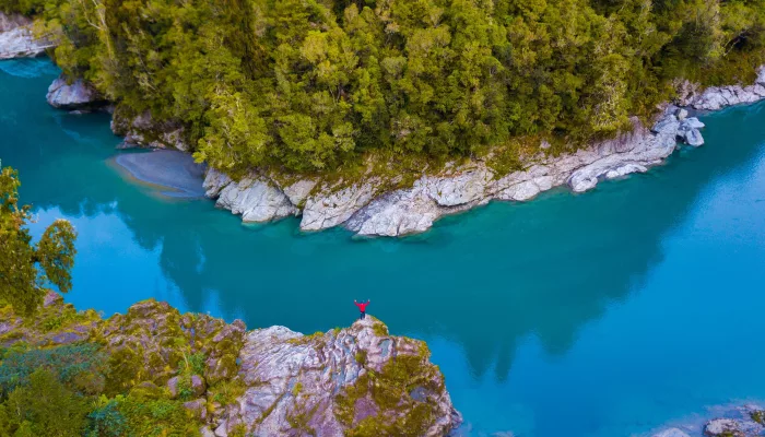 Person standing on rock ledge above the turquoise waters of Hokitika Gorge