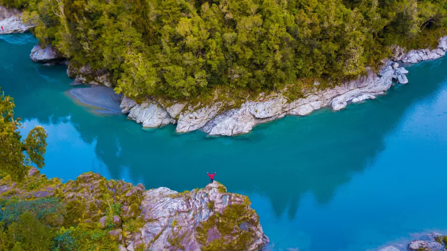 Person standing on rock ledge above the turquoise waters of Hokitika Gorge
