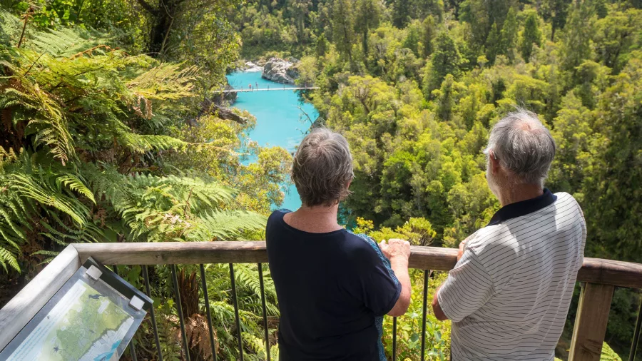 Two people at a lookout overlooking the turquoise Hokitika Gorge and swing bridge