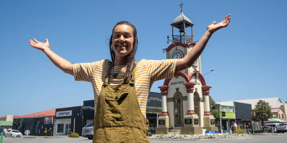 Smiling woman in front of the Hokitika Clock Tower on a sunny day