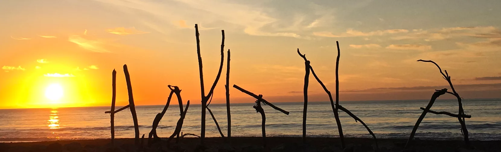 Driftwood sign spelling ‘Hokitika’ at sunset on the West Coast beach
