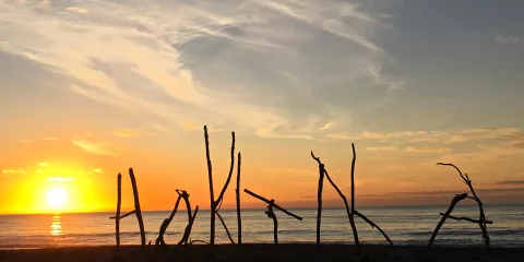 Driftwood sign spelling ‘Hokitika’ at sunset on the West Coast beach
