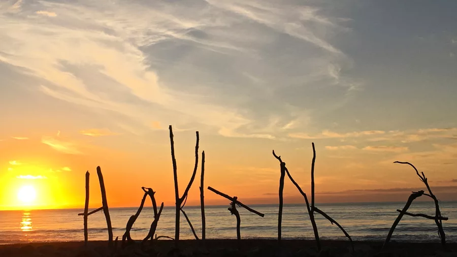 Driftwood sign spelling ‘Hokitika’ at sunset on the West Coast beach