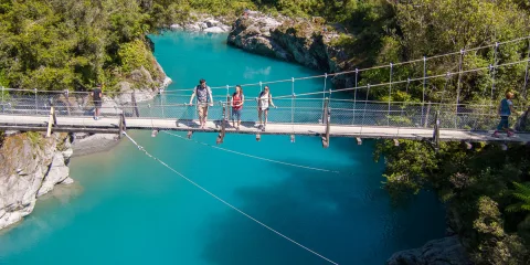 Visitors walking across the swing bridge above Hokitika Gorge’s vibrant blue river