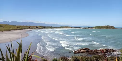 Waves breaking along the beach at Tauranga Bay, Cape Foulwind, with coastal headlands in the distance