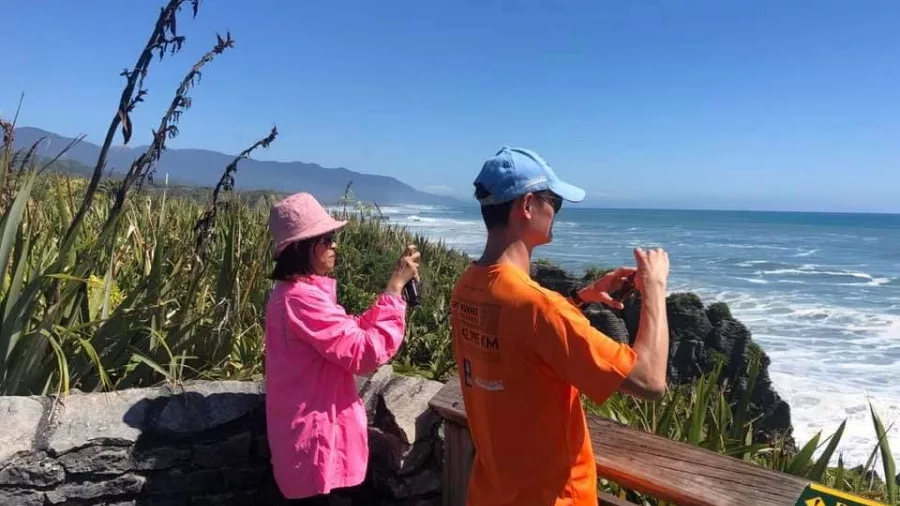 Tourists taking photos at a coastal viewing platform near the Punakaiki Blow Holes