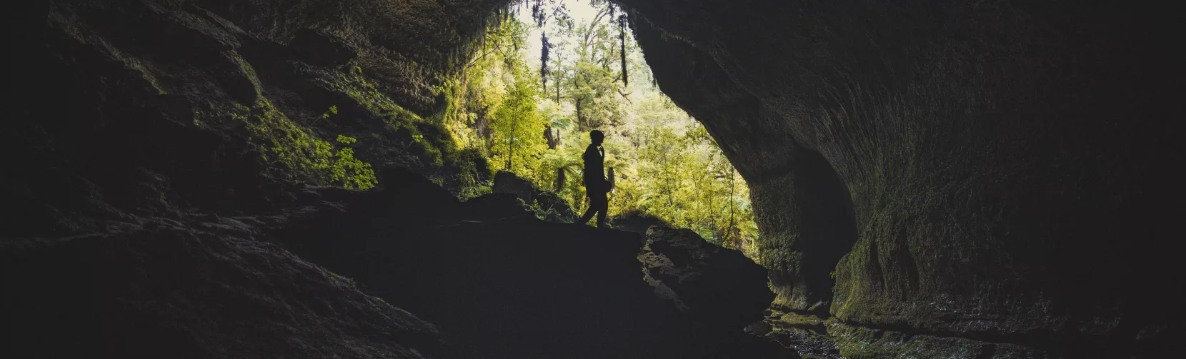 Silhouetted explorer at the entrance of Underworld Adventures cave in Charleston, West Coast NZ