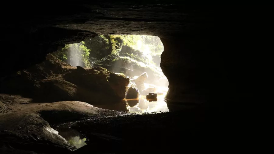 View from inside a limestone cave showing the illuminated entrance and rocky stream on the Glow Worm Cave Tour with Underworld Adventures in Charleston