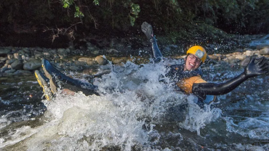 Person wearing a wetsuit and helmet splashing through a rapid during Underworld Rafting in Charleston, New Zealand.