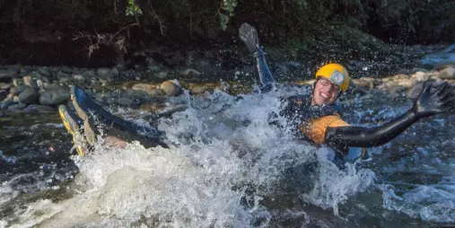 Person wearing a wetsuit and helmet splashing through a rapid during Underworld Rafting in Charleston, New Zealand.