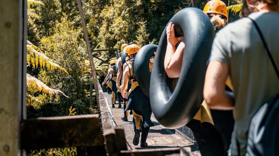 Group of adventurers carrying tubes and walking across a suspension bridge in Charleston forest