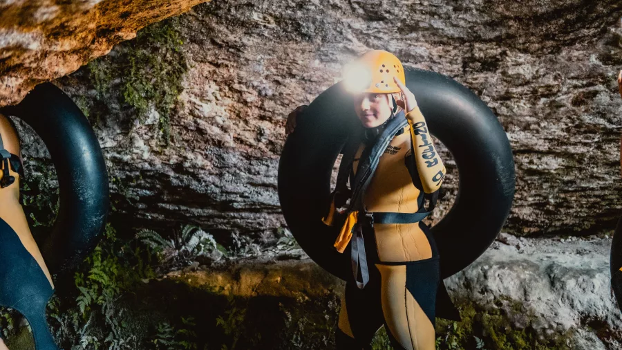 Person in wetsuit and helmet carrying a tube inside a cave at Underworld Adventures Charleston