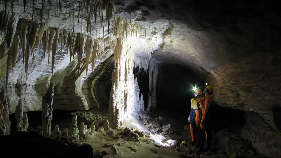 Two cavers explore a glow-lit limestone cave with stalactites in Charleston