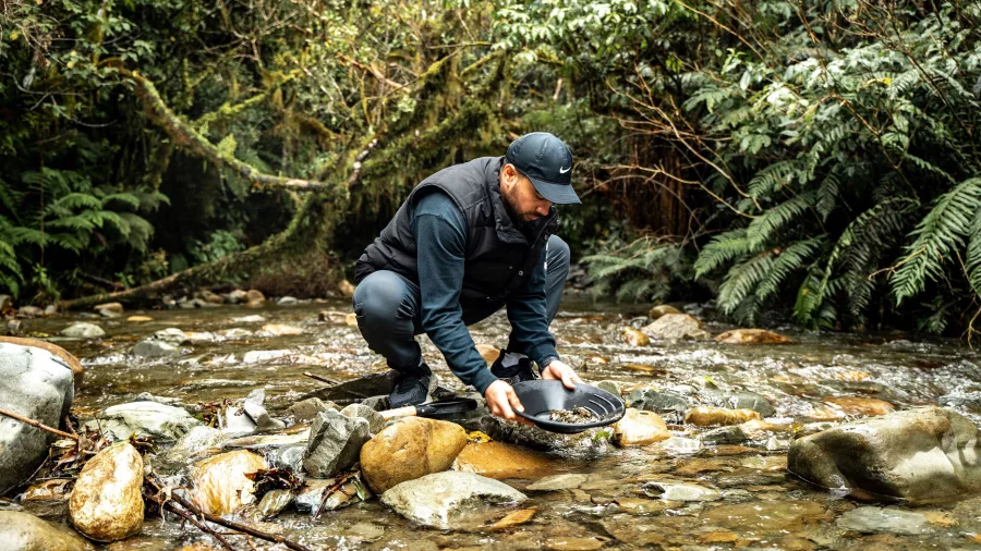 Man crouched in a creek panning for gold in Ross on the West Coast of New Zealand