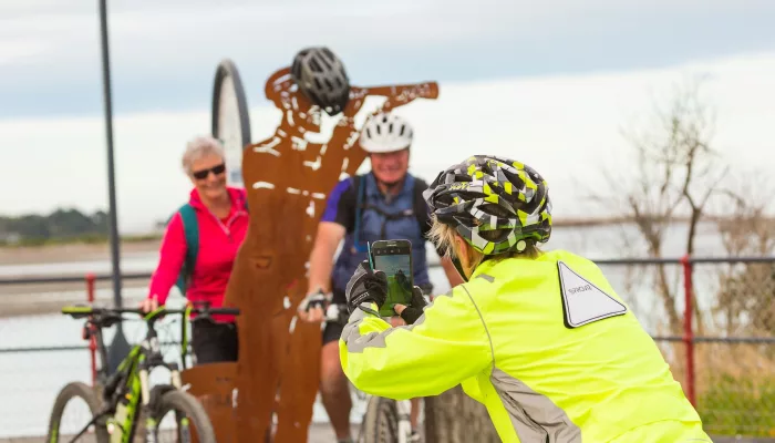 Cyclists taking a photo by a sculpture along the Hokitika River on the West Coast Wilderness Trail