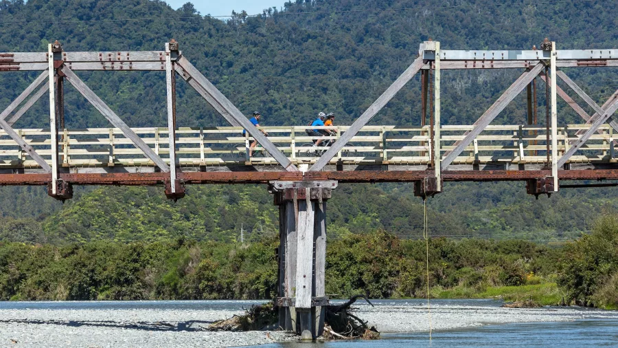 Cyclists crossing the full span of Tōtara Bridge on the West Coast Wilderness Trail
