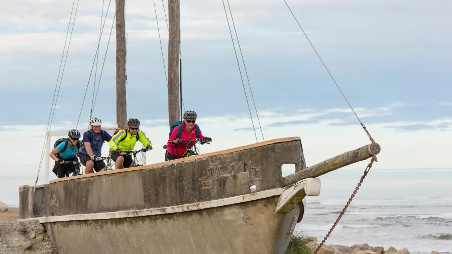 Cyclists riding past the replica ship Tambo at Sunset Point in Hokitika on New Zealand’s West Coast