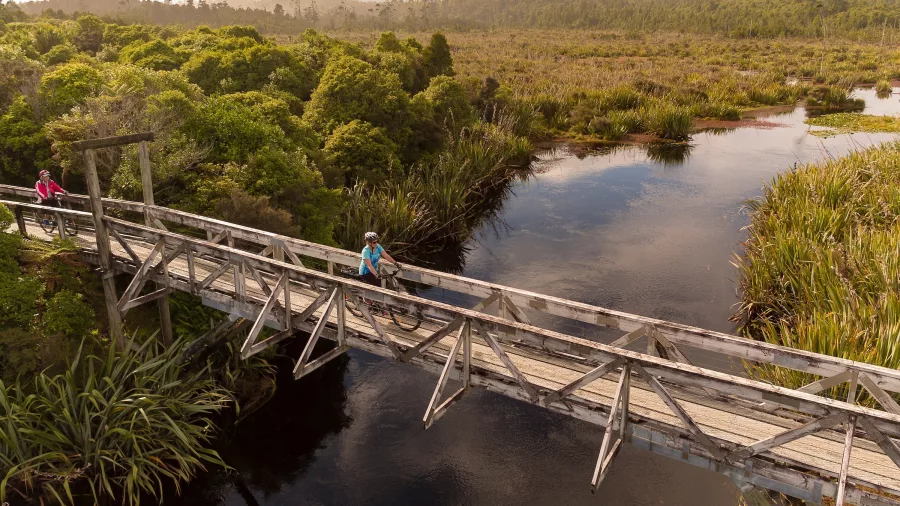 Cyclists walking across the Mahinapua Bridge on the West Coast Wilderness Trail