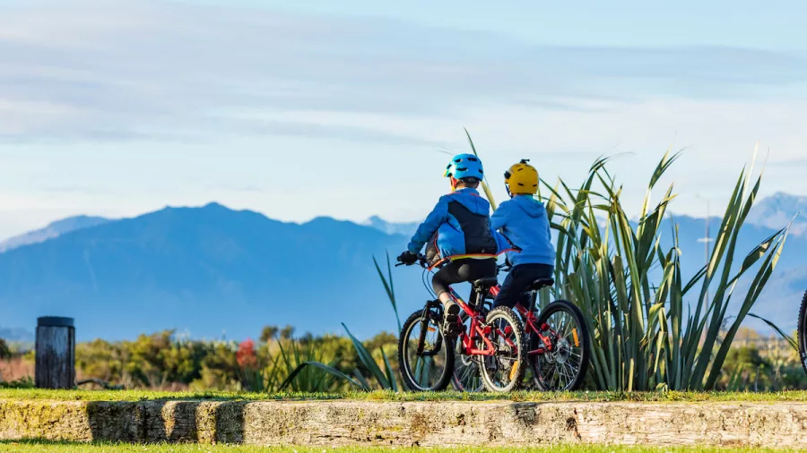 Two children cycling with mountain views along the West Coast Wilderness Trail in New Zealand