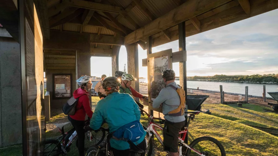 Cyclists reading interpretive panels at the reconstructed miners’ bathhouse in Coal River Park along the Greymouth Floodwall