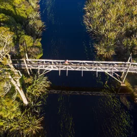 Cyclist crossing the wooden bridge over Māhinapua Creek near Hokitika on the West Coast Wilderness Trail