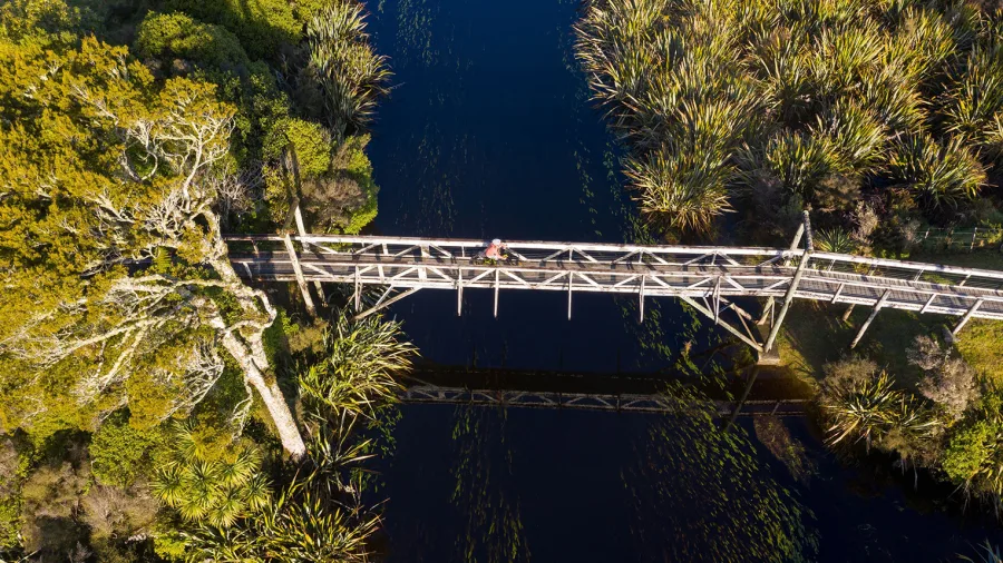 Cyclist crossing the wooden bridge over Māhinapua Creek near Hokitika on the West Coast Wilderness Trail
