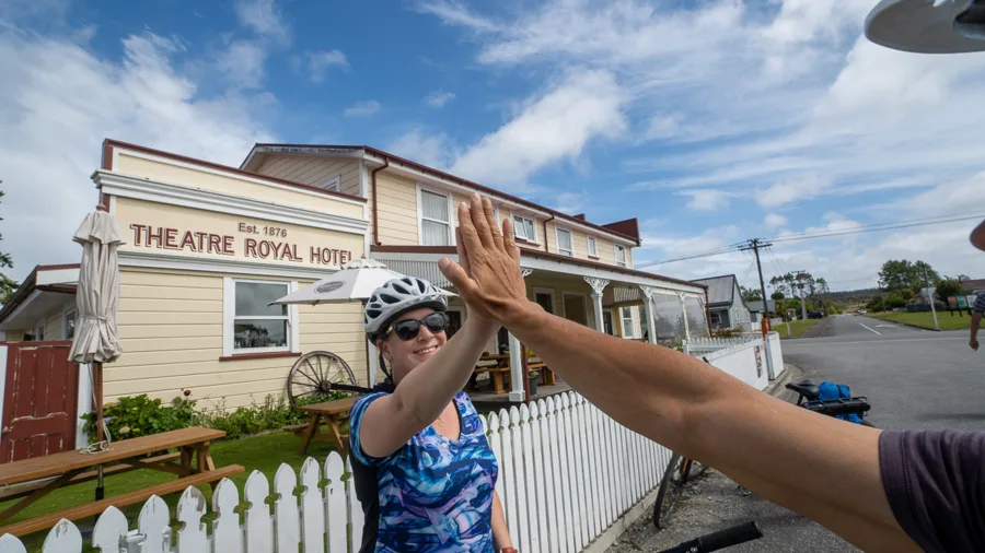 Cyclists high-fiving outside Theatre Royal Hotel in Kumara on the West Coast Wilderness Trail