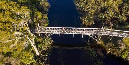 Cyclist crossing the wooden bridge over Māhinapua Creek near Hokitika on the West Coast Wilderness Trail